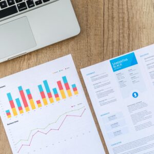 Top view of a laptop, charts, and resume on a wooden desk, showcasing business analysis and job application.