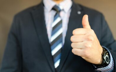 Close-up of a businessman in a suit giving a thumbs up gesture, symbolizing success.